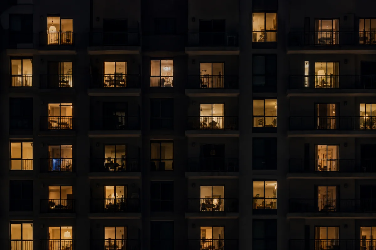 The facade of an apartment building at night, dozens of units lit from within